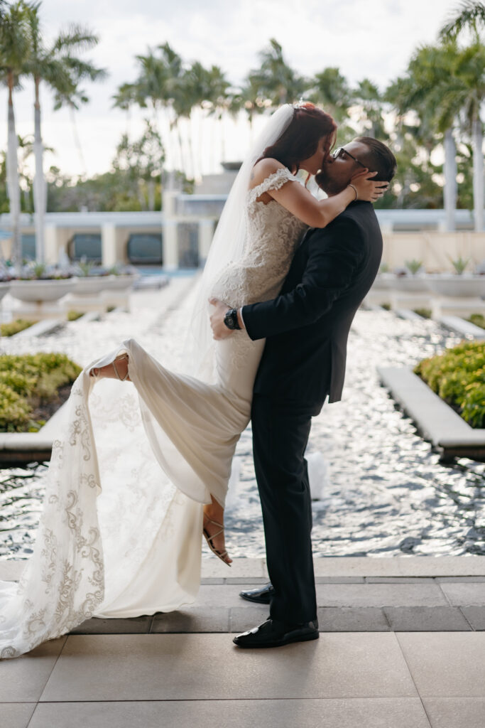 Groom lifts bride for bridal portraits in front of a stunning fountain view at the Hyatt Regency Coconut point in Estero, Florida. 