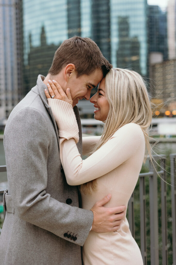 Couple embracing in front of Downtown Chicago river at Gibson's Italia in Chicago, Illinois during their engagement photoshoot. 