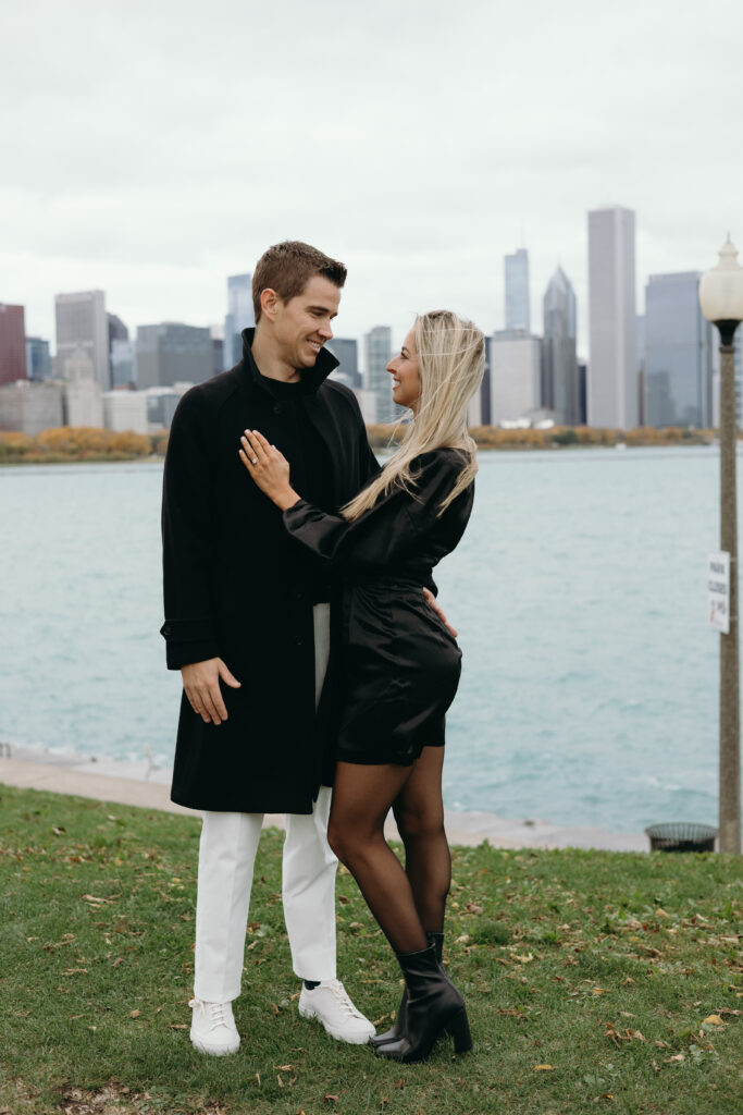 Couple embracing each other and showing engagement ring at Northerly Island in Chicago, Illinois during engagement photoshoot. 