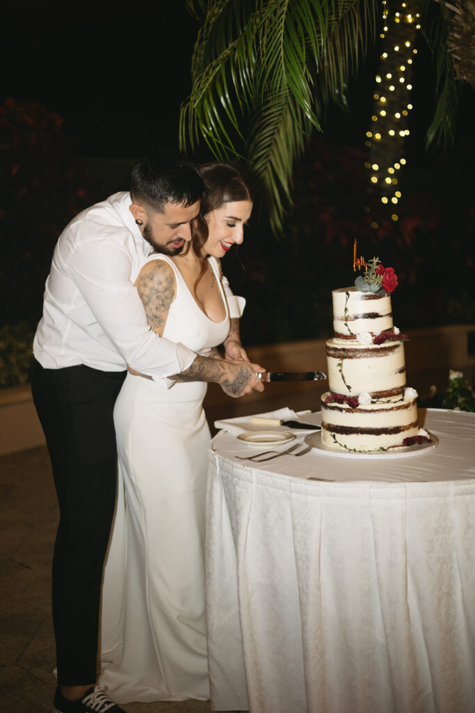 Bride and groom happily cut their wedding cake during their wedding reception at The Club at the Strand in Naples, Florida. 