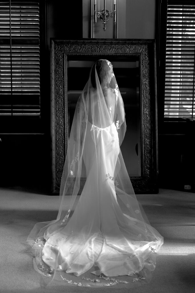 Bride posing in front of a mirror in getting ready suite during wedding at The Club at the Strand in Naples, Florida. 