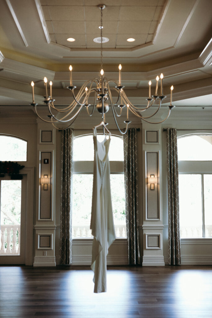 Brides dress hanging on chandelier during wedding at The Club at the Strand in Naples, Florida. 